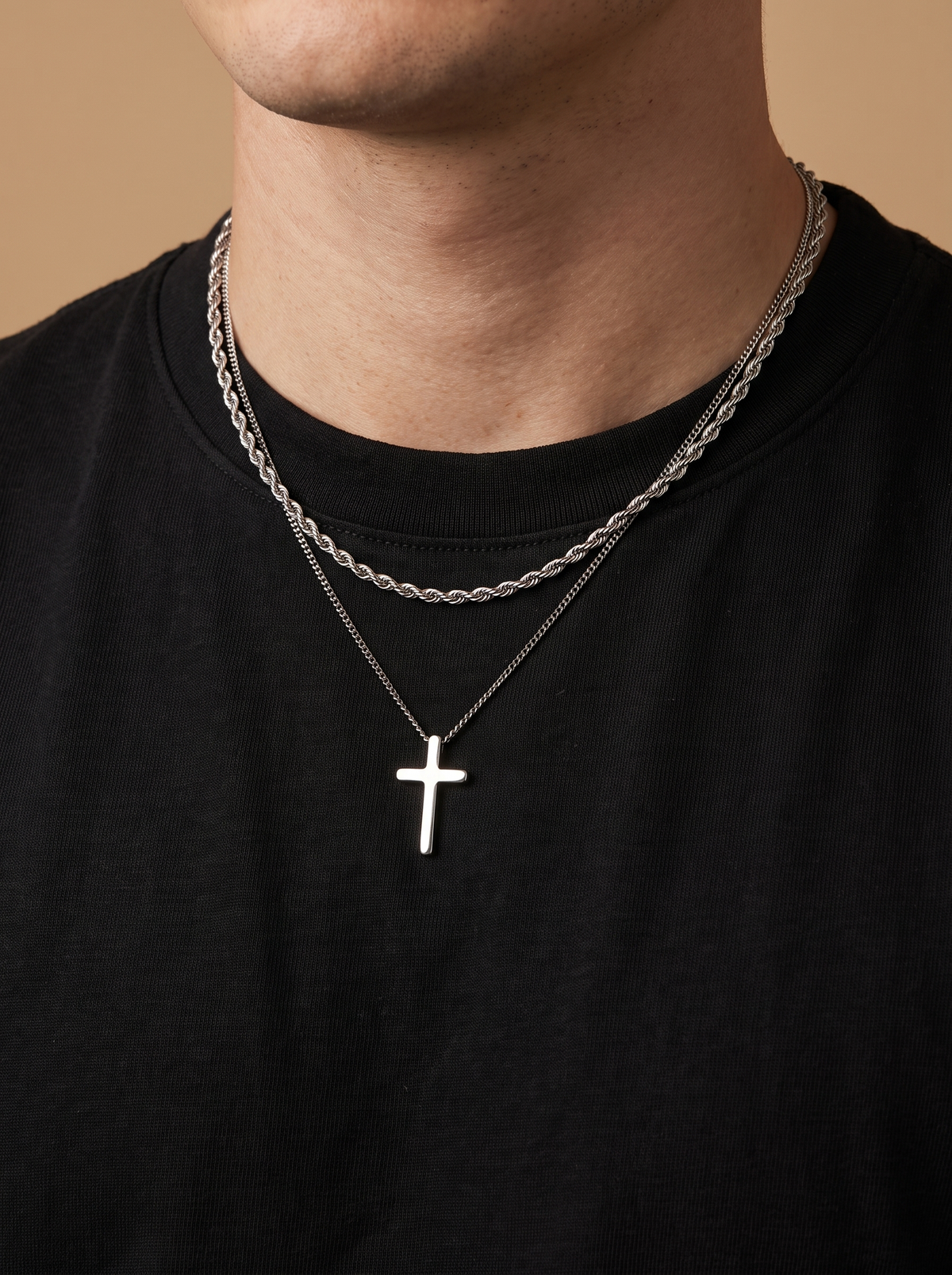 Silver cross necklace and rope chain worn over a black t-shirt