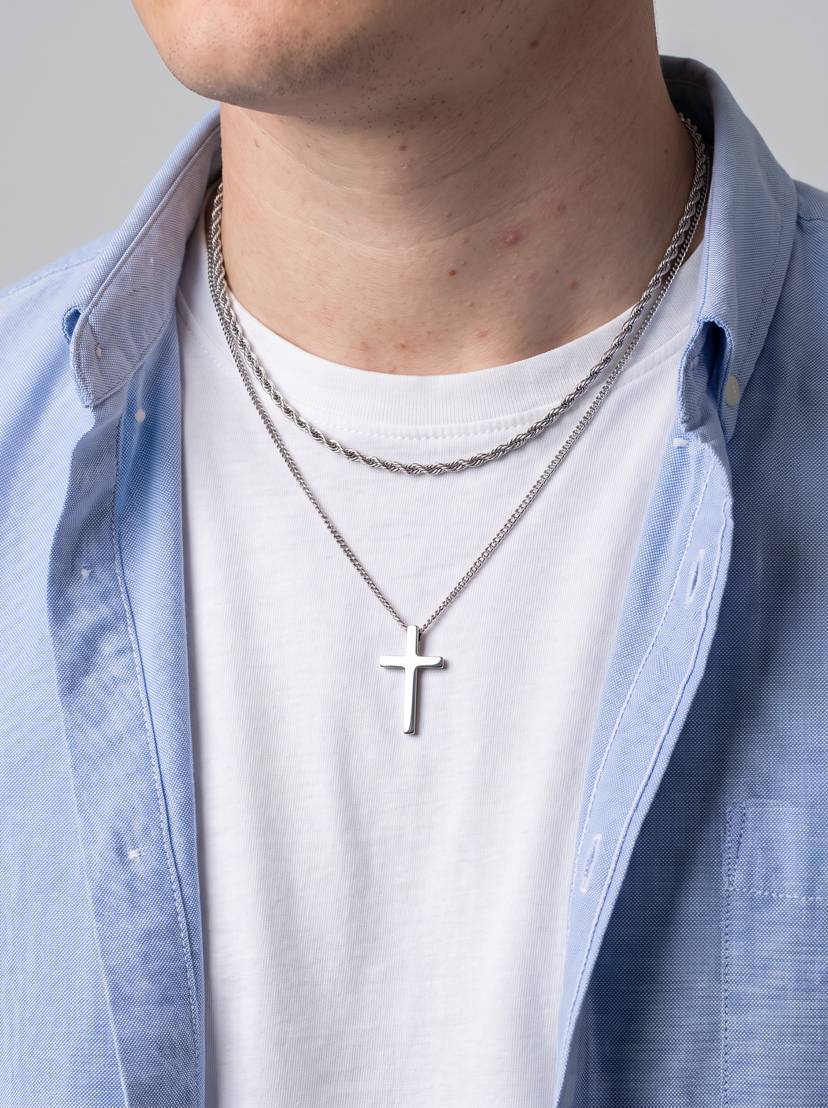 Silver cross necklace and rope chain worn over a white tee under an open oxford shirt